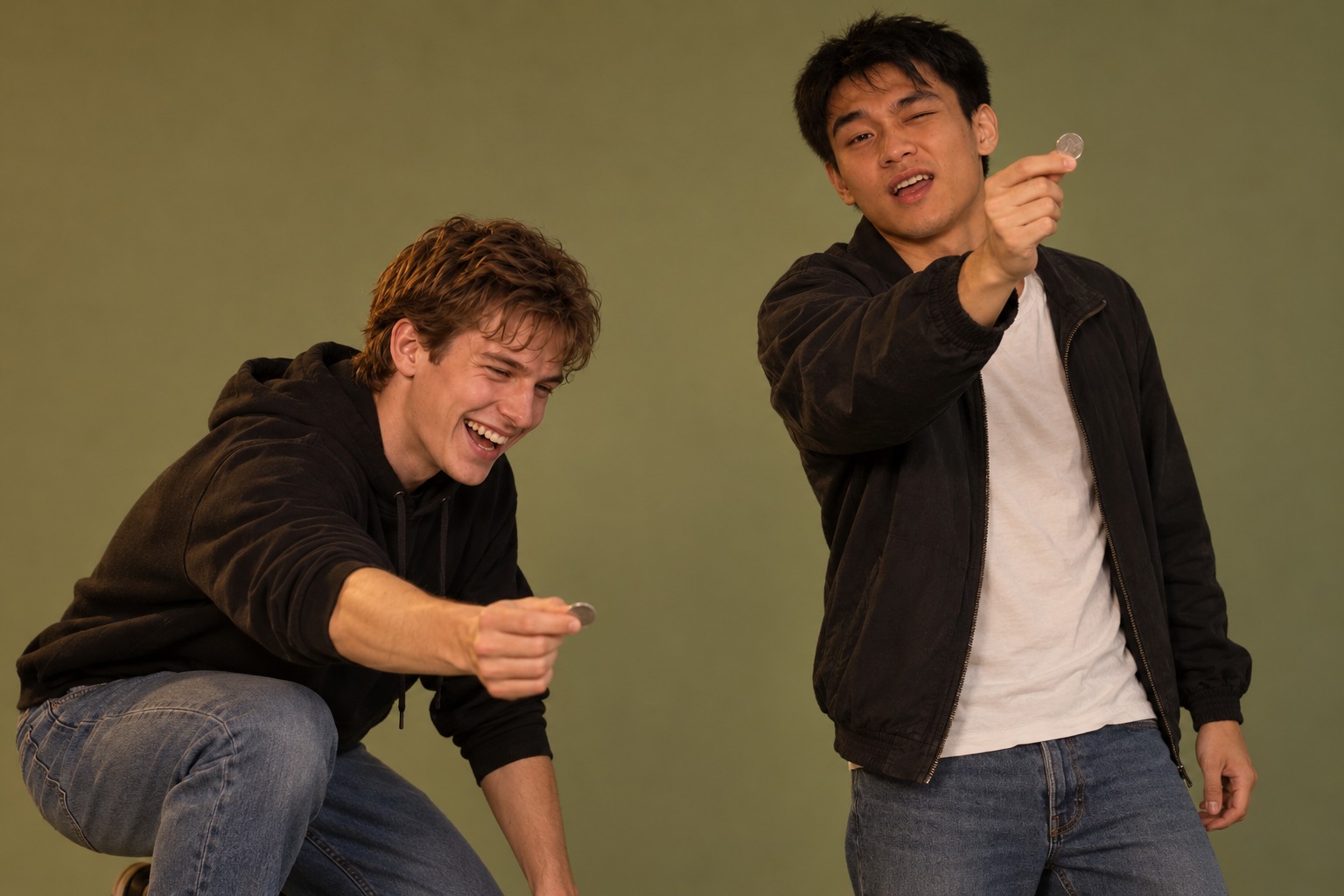 Two guys in a casual coin throwing contest, one crouching and one standing tall with a coin held up to aim.