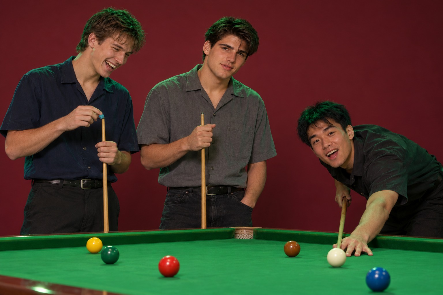 Three young men around a snooker table, one bending low to line up a shot while two watch with smirks.