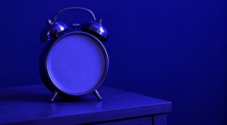 Plain wind-up alarm clock on a bedside table in indigo light