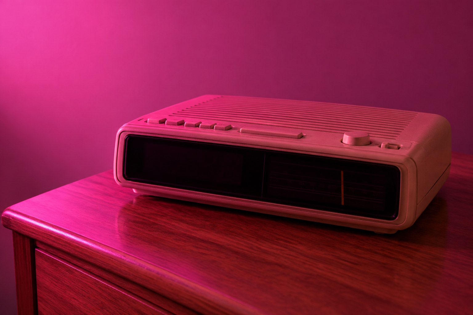 A beige 1990s clock radio with a dark display on a bedside table in pink light