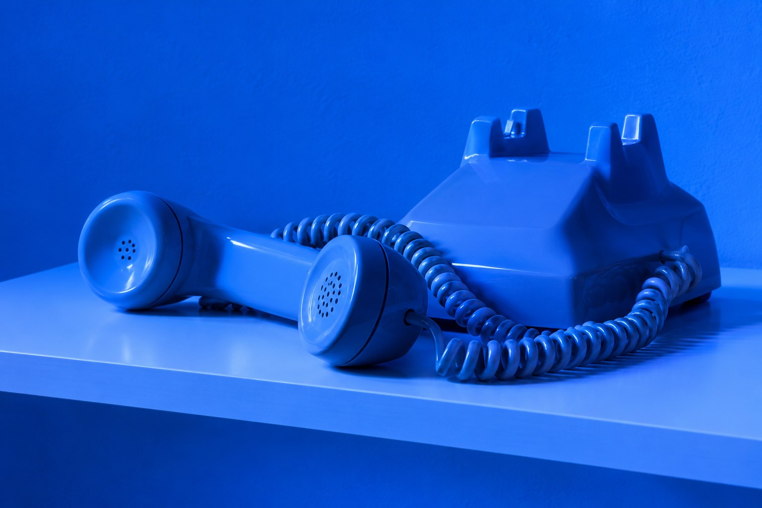 A beige corded telephone with a curly cord on a wooden table in cool blue light