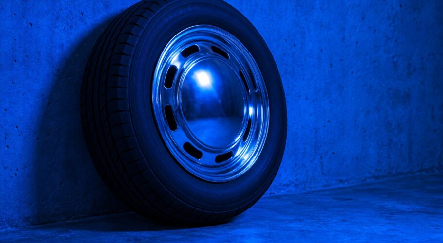 A black car tyre with a chrome hubcap leaning on a concrete wall