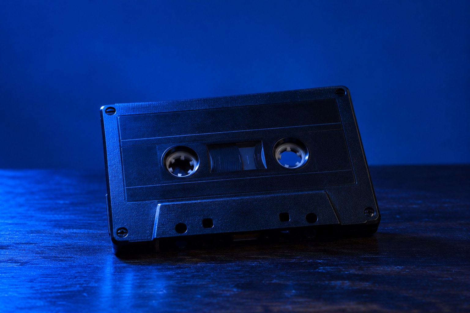 A black cassette tape resting on a dark wooden table under blue light