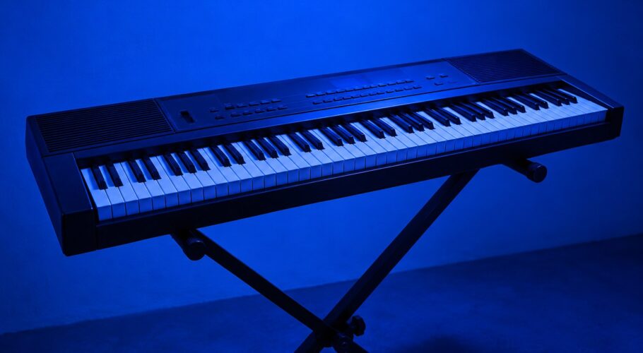A black 1990s electric keyboard piano on a stand in blue light