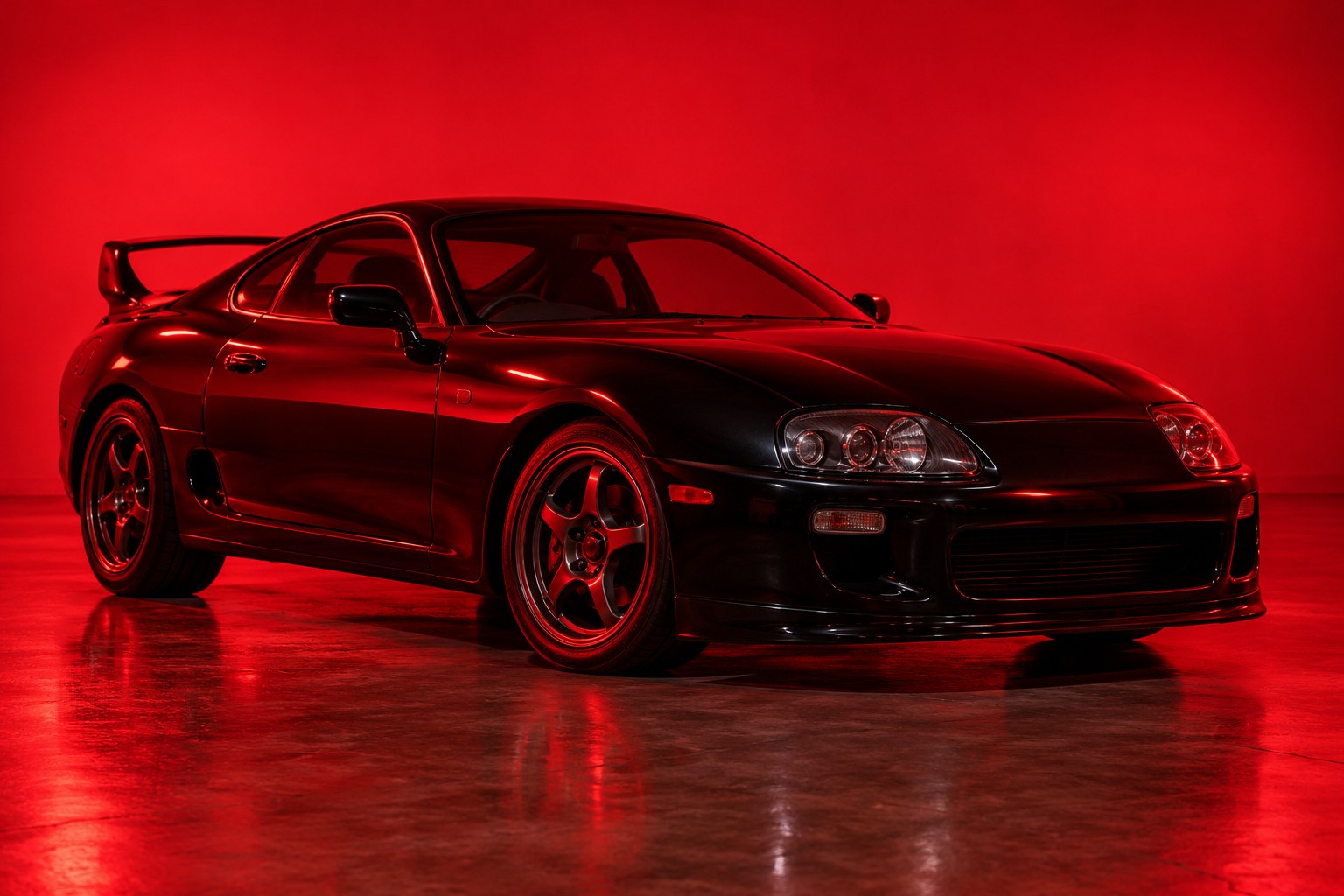 A black 1990s sports coupe parked on a bare concrete floor under red light
