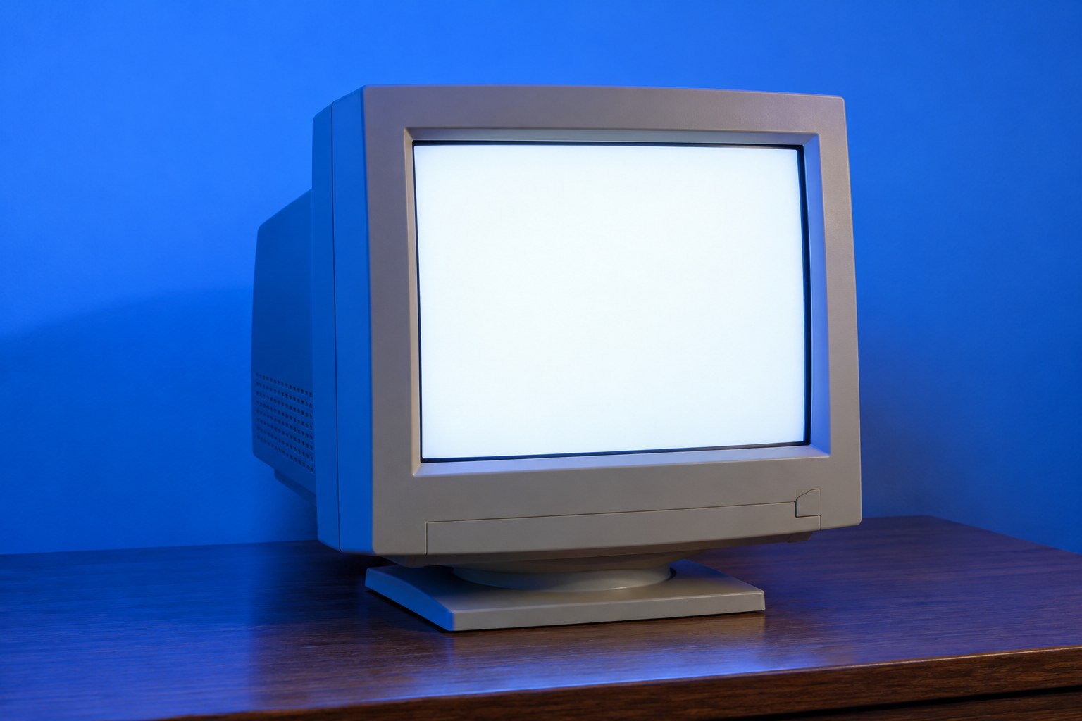 A beige CRT computer monitor glowing with a blank page on a wooden desk in blue light