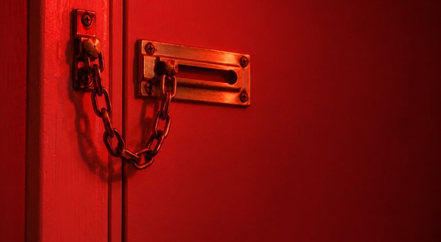 A brass door chain lock on a plain wooden door frame