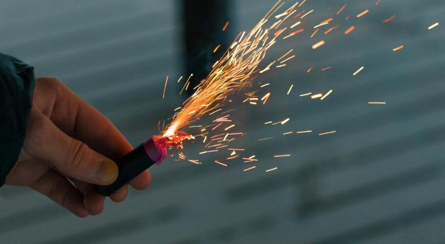 a guy holding a burning a firecracker with sparks