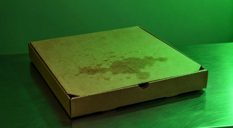 A closed cardboard pizza box on a steel bench in green light