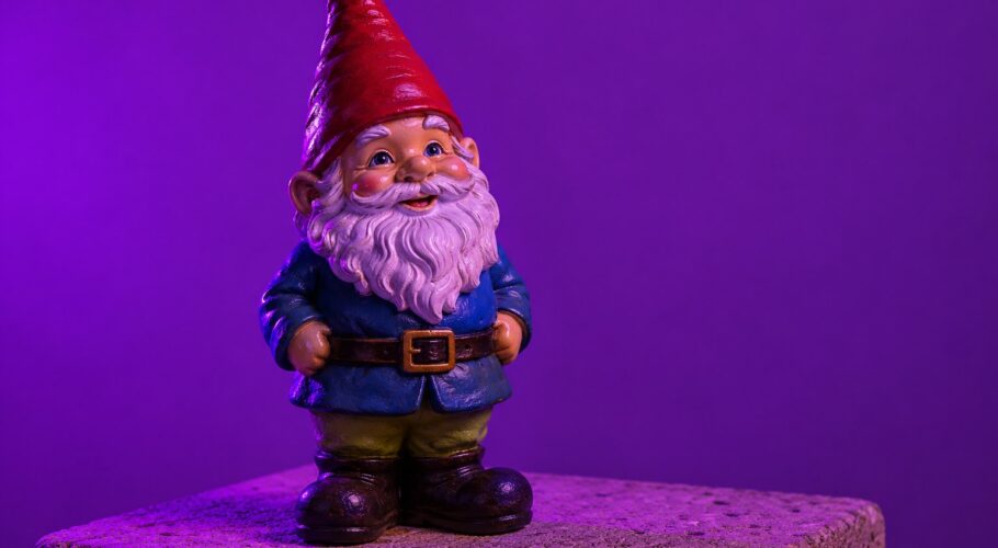 A ceramic garden gnome with a red hat on a concrete paver in purple light