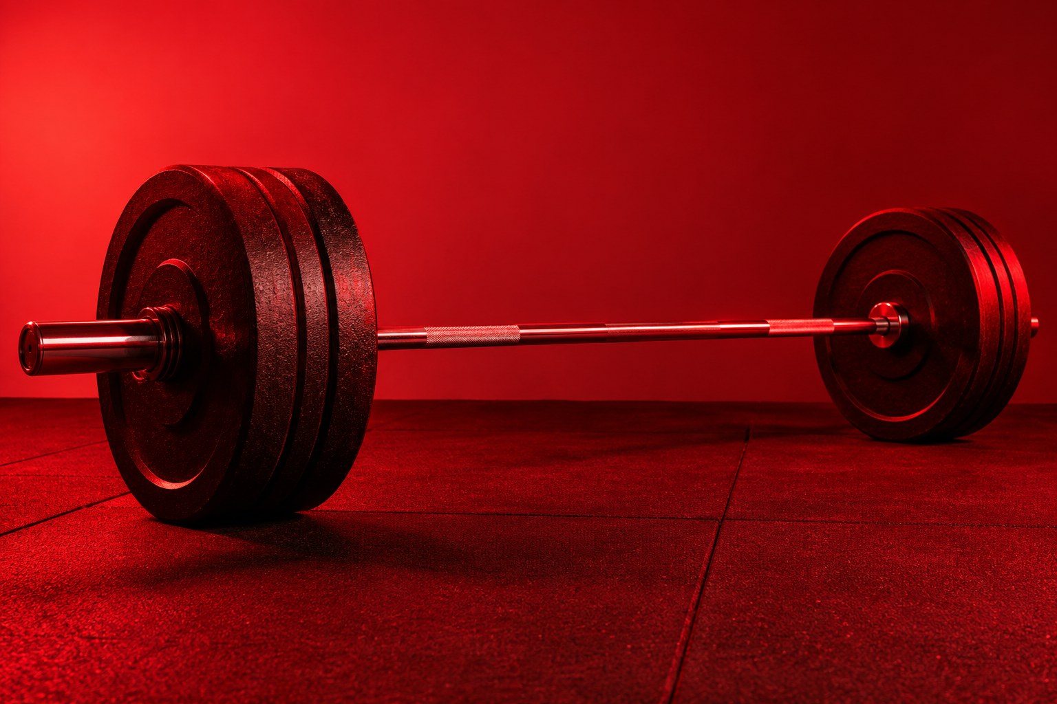 A chrome barbell loaded with black cast-iron weight plates resting on a rubber gym floor under red light