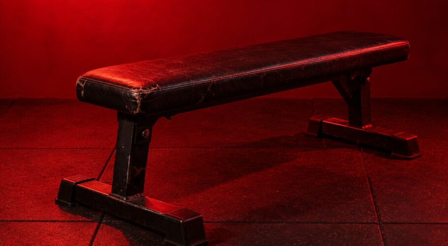 A chrome barbell loaded with cast iron weight plates on a rubber gym floor in red light