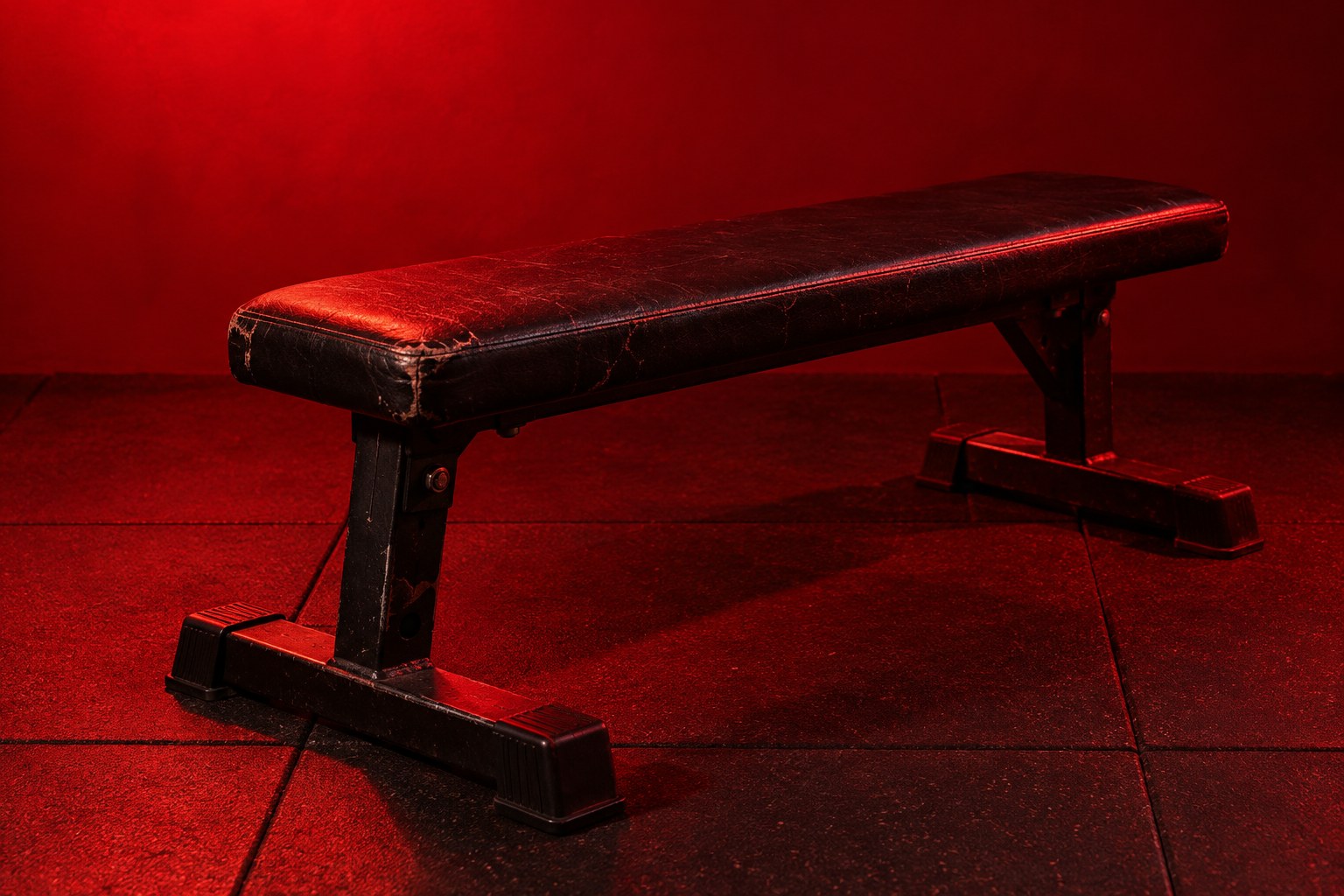A chrome barbell loaded with cast iron weight plates on a rubber gym floor in red light