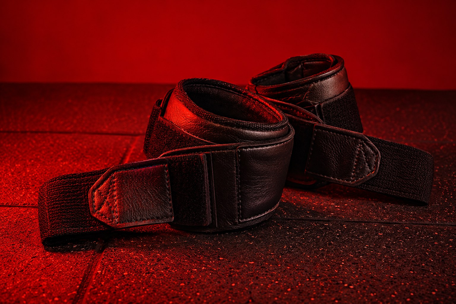 A chrome dumbbell resting on a black rubber gym mat under red light