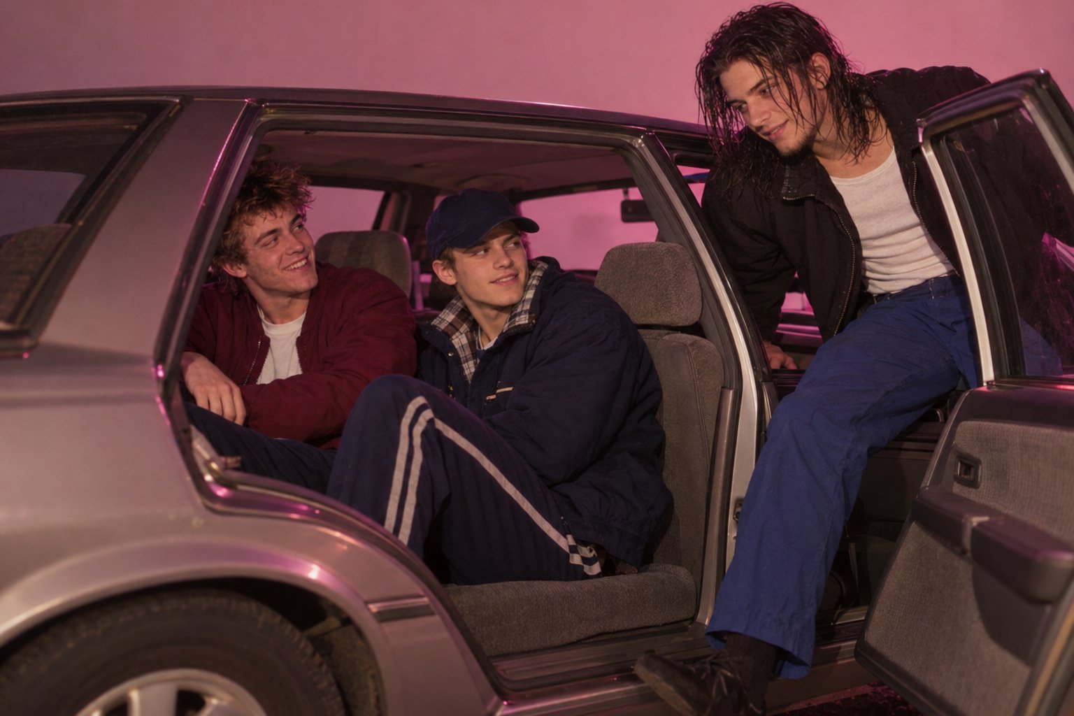 A young man in a black jacket climbs into the back of a parked sedan where two friends greet him at night.