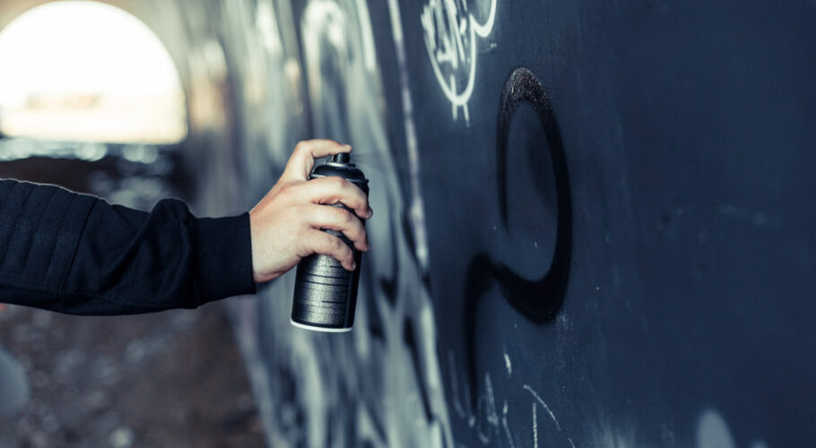 close up persons hand spraying paint with aerosol can graffiti wall