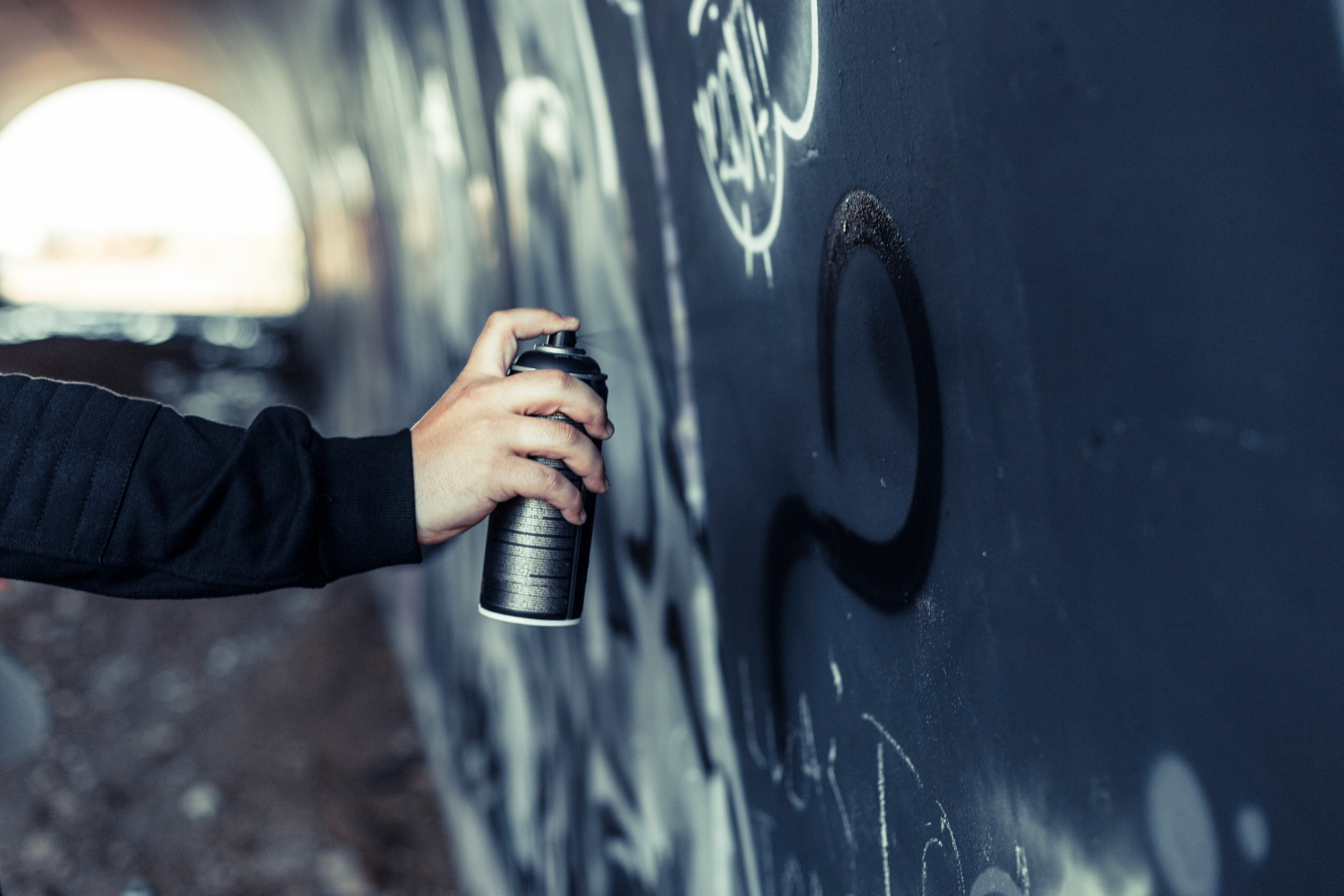 close up persons hand spraying paint with aerosol can graffiti wall
