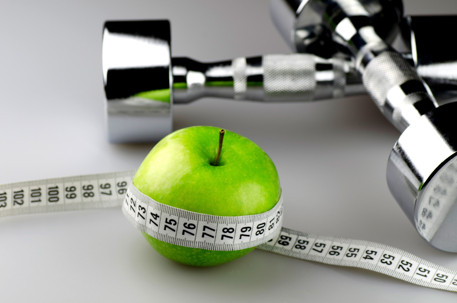 dumbbells with measuring tape apple diet concept background