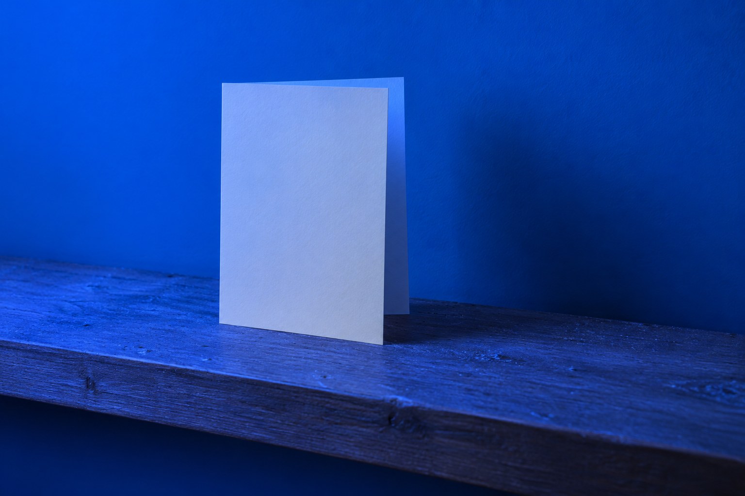 A lone blank greeting card standing on a dusty wooden shelf in blue light