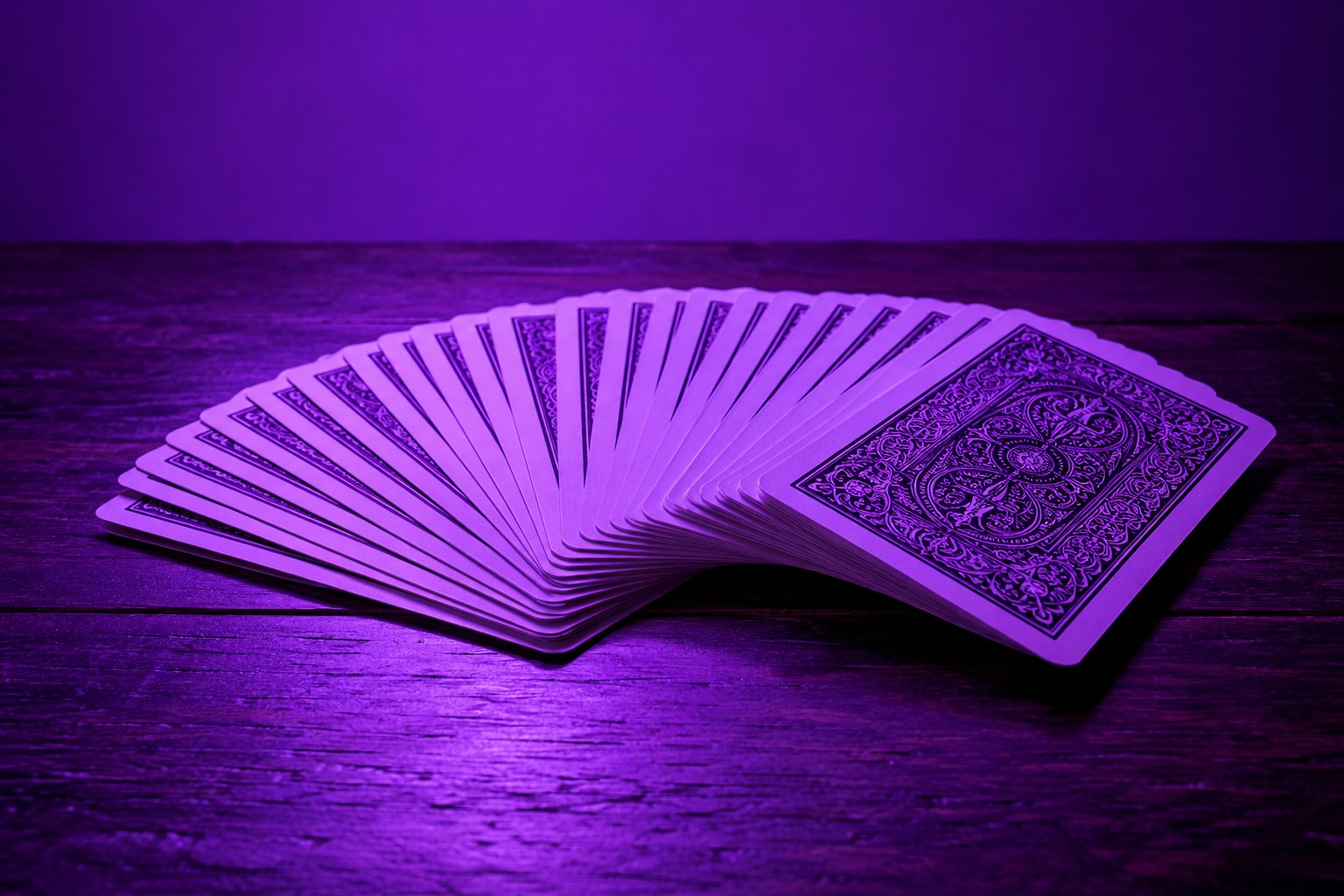 A fanned deck of playing cards on a dark wooden table in violet light