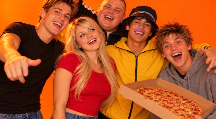 Five young friends cheering with a pizza box against a plain orange studio backdrop