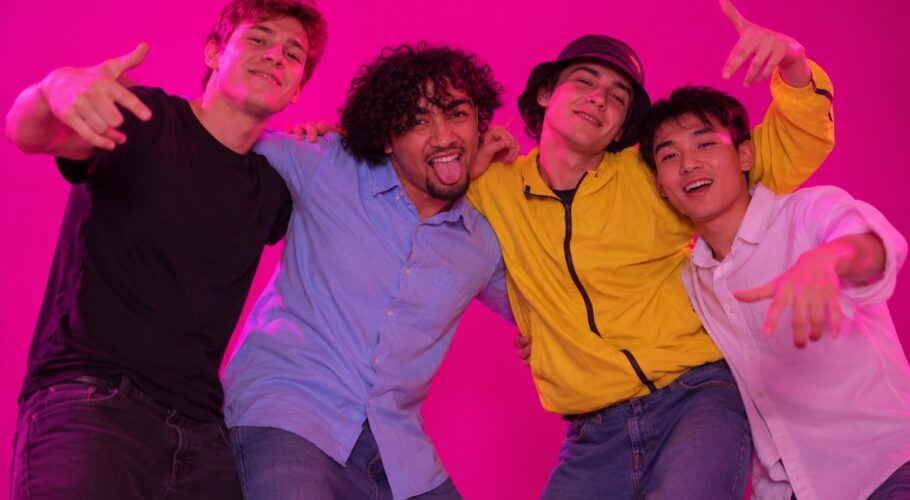 Four young guys with arms over shoulders dancing and laughing against a plain magenta studio backdrop