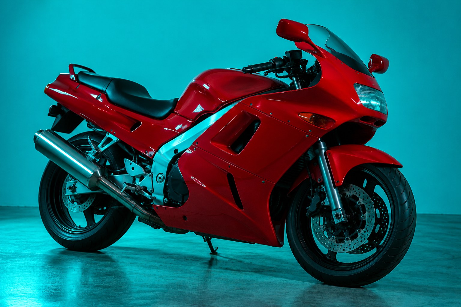 A glossy red 1990s Japanese road motorbike on a concrete floor under cyan light