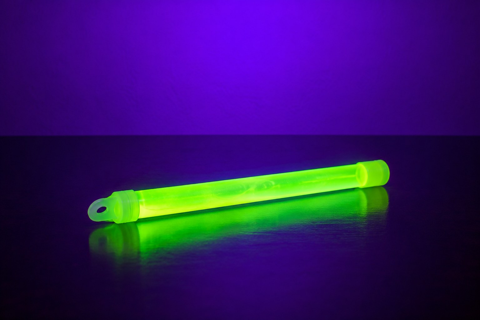 A neon green glow stick on a dark glossy table in violet light