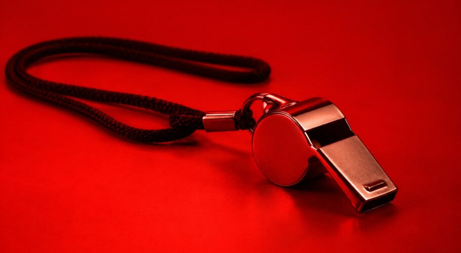 a plain silver referee whistle on a black cord photographed in a studio