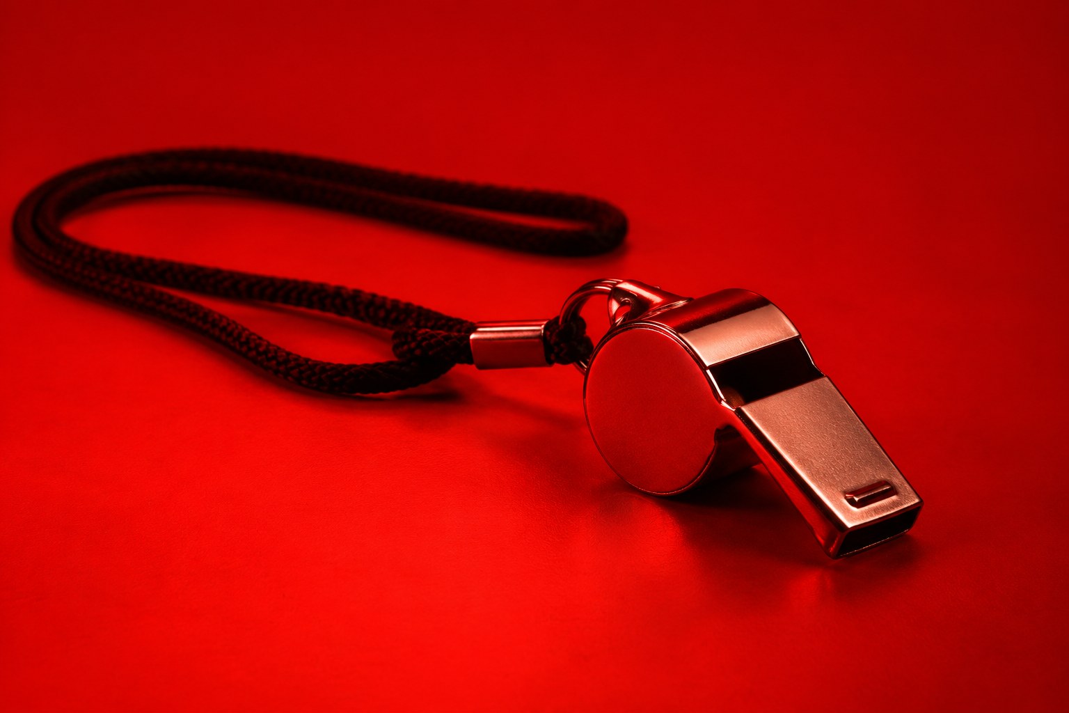 a plain silver referee whistle on a black cord photographed in a studio