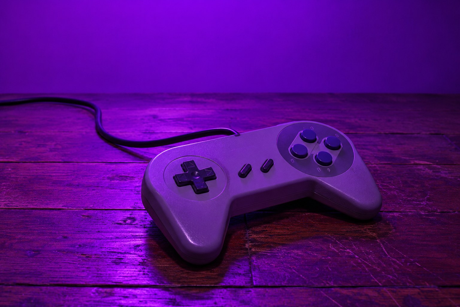 A grey 1990s game controller on a wooden floor under purple light