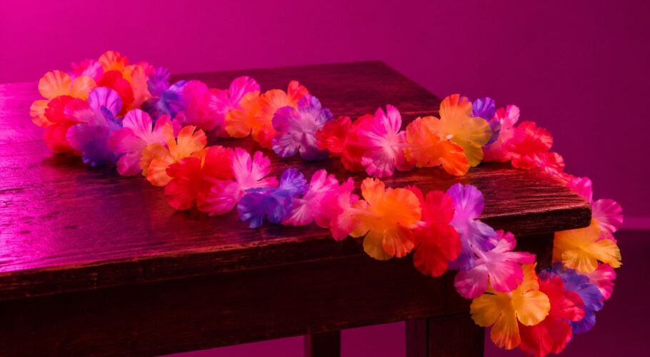 A garland of bright plastic Hawaiian flowers on a dark wooden table in magenta light