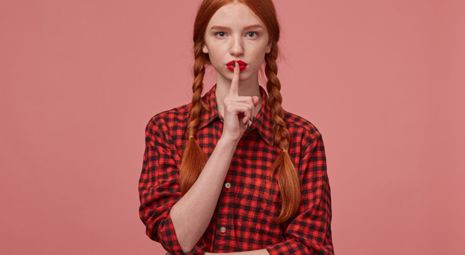 indoor shot serious ginger female showing silence gesture kathryn