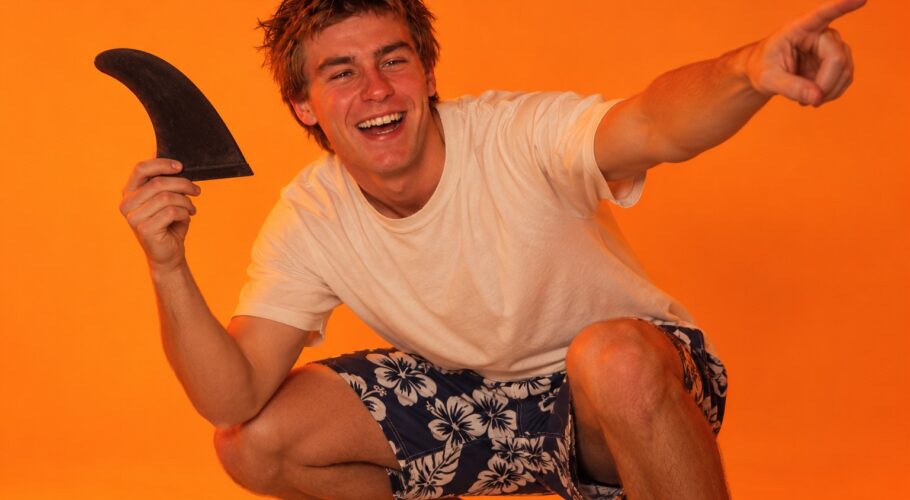 Jett crouching with a surfboard fin pointing excitedly at the beach