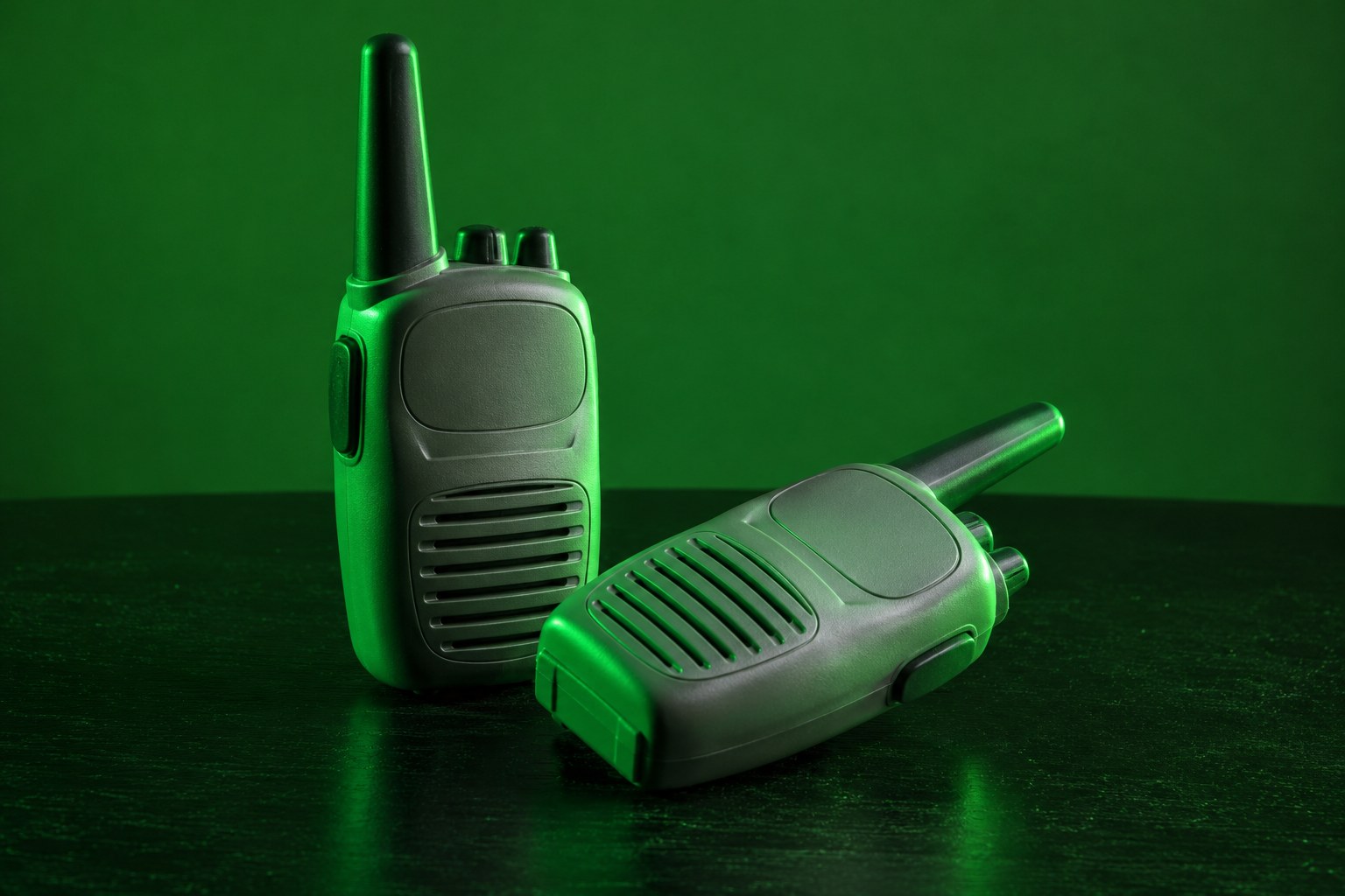 a pair of grey plastic toy walkie talkies with short antennas on a black table photographed in a studio