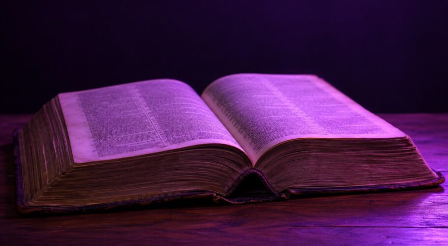 An old open dictionary on a wooden table under purple light