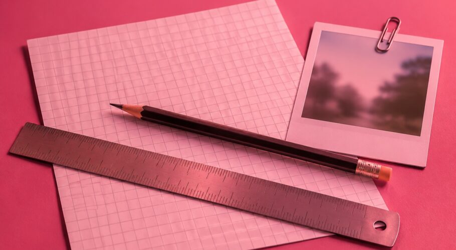 A pencil and ruler over a gridded drawing sheet beside a clipped photograph