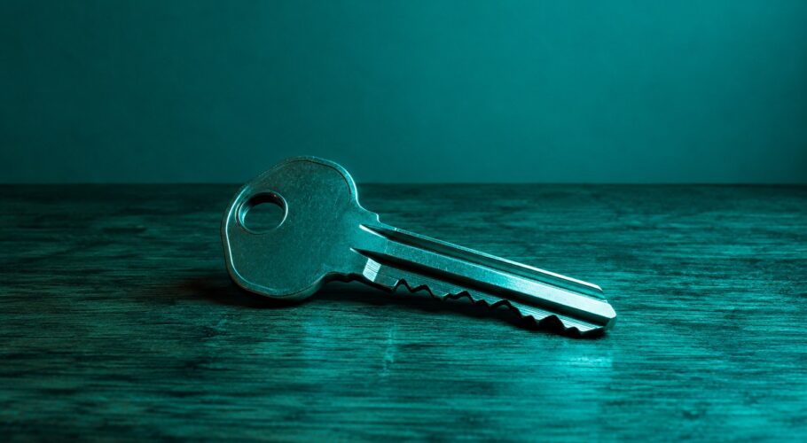 A plain metal house key lying on a wooden table in teal light