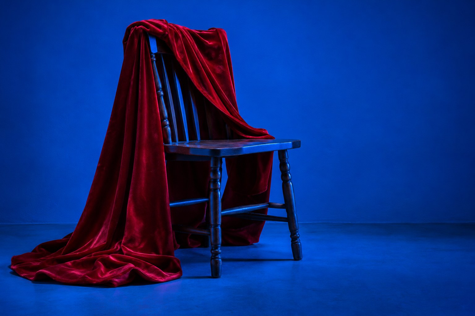 A plain red cape draped over the back of a wooden chair in blue light