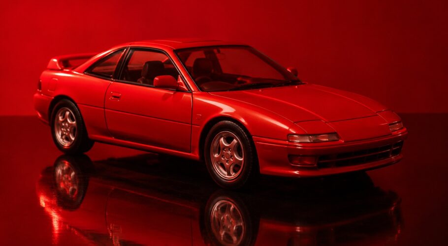 A small red toy coupe sitting on a shiny black surface