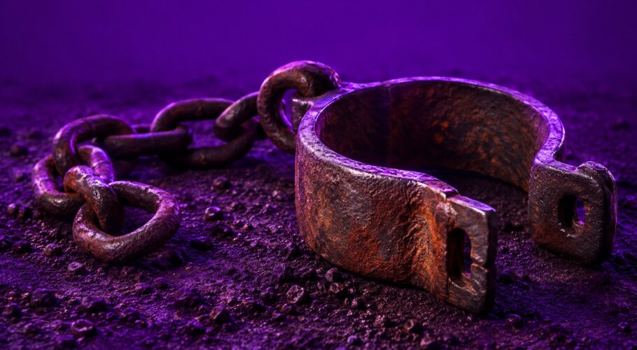 A rusted iron shackle and chain lying on dark soil