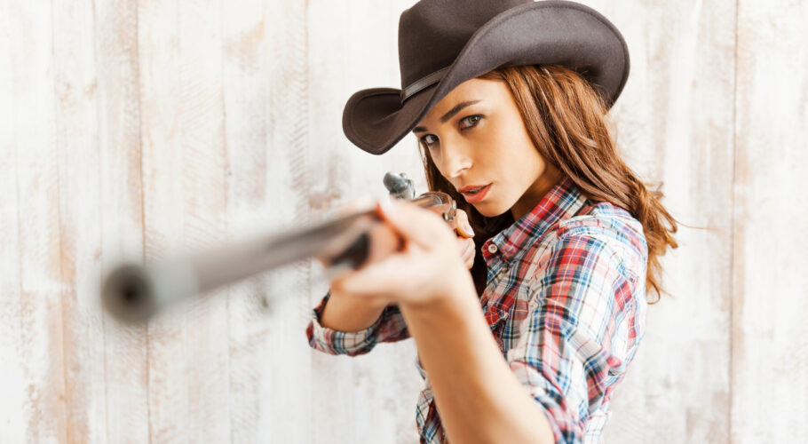 shoot straight beautiful young blonde cowgirl aiming her gun while standing against wooden background