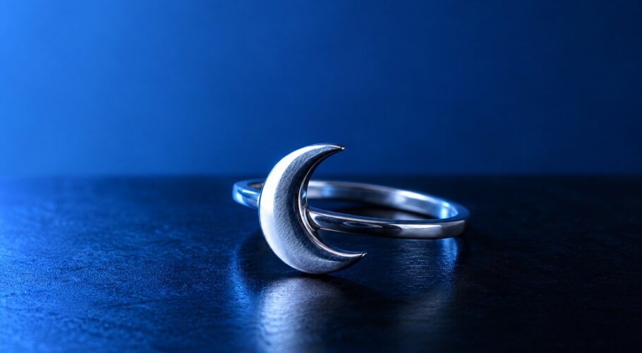 A plain silver ring with a crescent moon design on a black surface in pale blue light