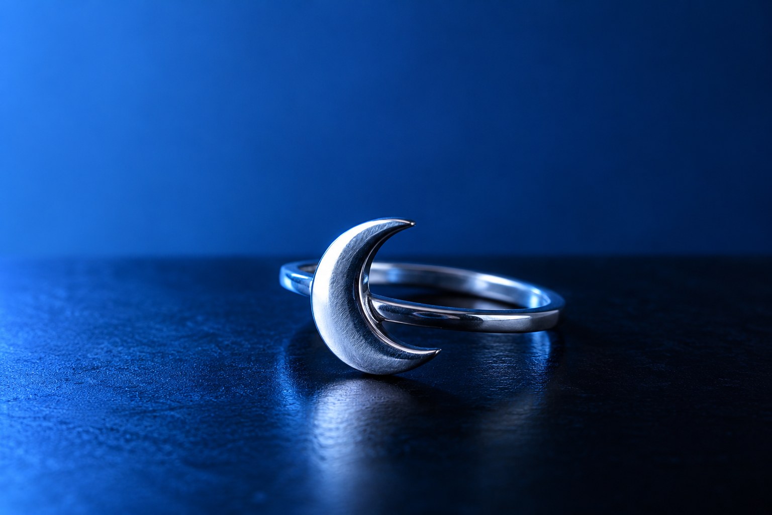 A plain silver ring with a crescent moon design on a black surface in pale blue light