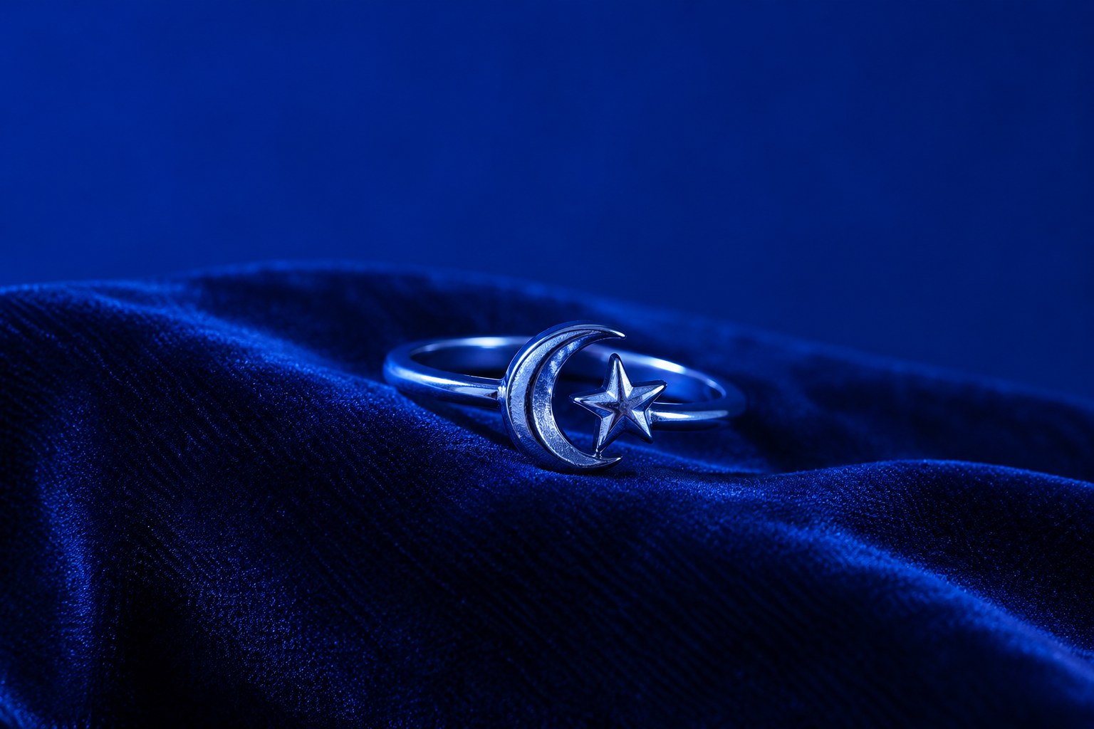 A small silver star and crescent moon ring on dark velvet
