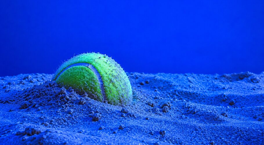 Tennis ball half buried in sand in blue light