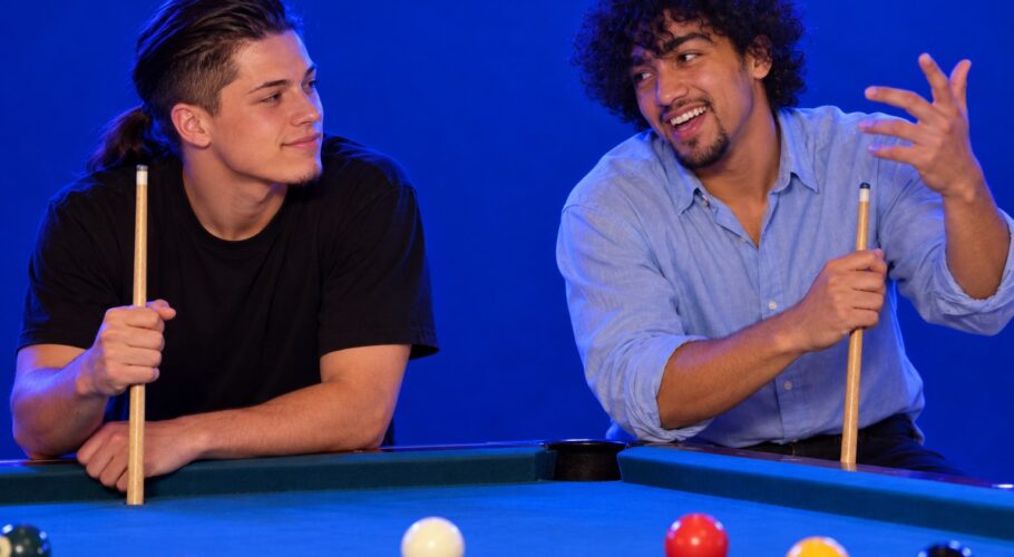 Tony and Ralf leaning on a pool table with cues while Ralf tells a tall story, 1999