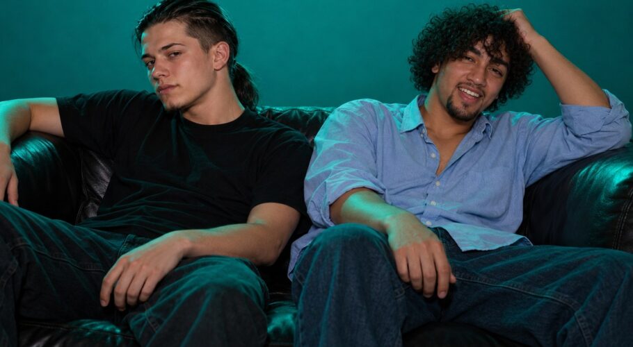 Ralf and Tony slumped, worn out, on a dark nightclub sofa