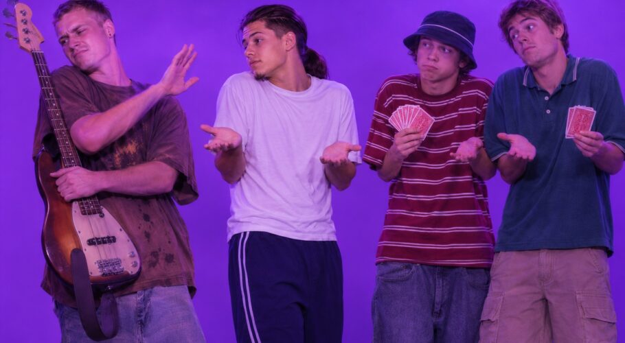Tony in a white tee shrugging beside Keith with a bass guitar and two friends holding cards, April 1999