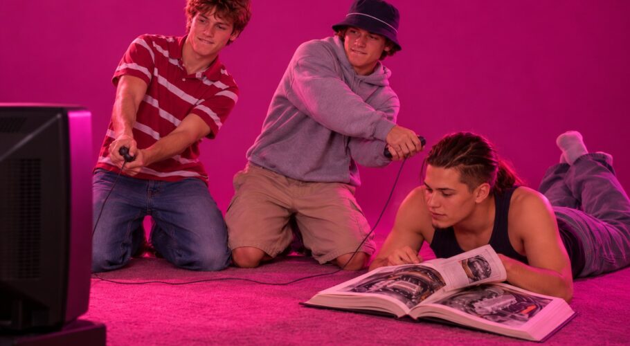 Tony lying on his front reading a book while two friends play a console game, March 1999